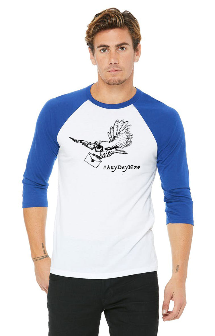 A man wearing a white and blue baseball tee with a graphic of a bird and the text "#AnyDayNow" printed on it.