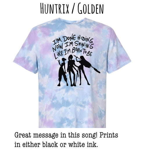 A tie-dye t-shirt with a graphic design featuring silhouettes of three people and text that reads "I'm done hiding now I'm shining like I'm born to be".