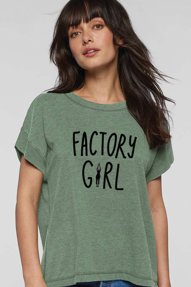 A woman with long dark hair wearing a green t-shirt with the text "FACTORY GIRL" printed on it.