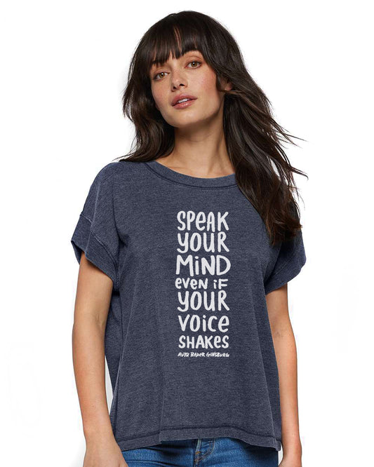 A woman with long dark hair wearing a gray t-shirt with white text that says "SPEAK YOUR MIND EVEN IF YOUR VOICE SHAKES".