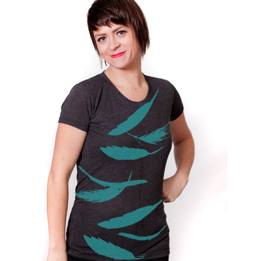 A woman wearing a gray t-shirt with a graphic design of green feathers on it, smiling at the camera.