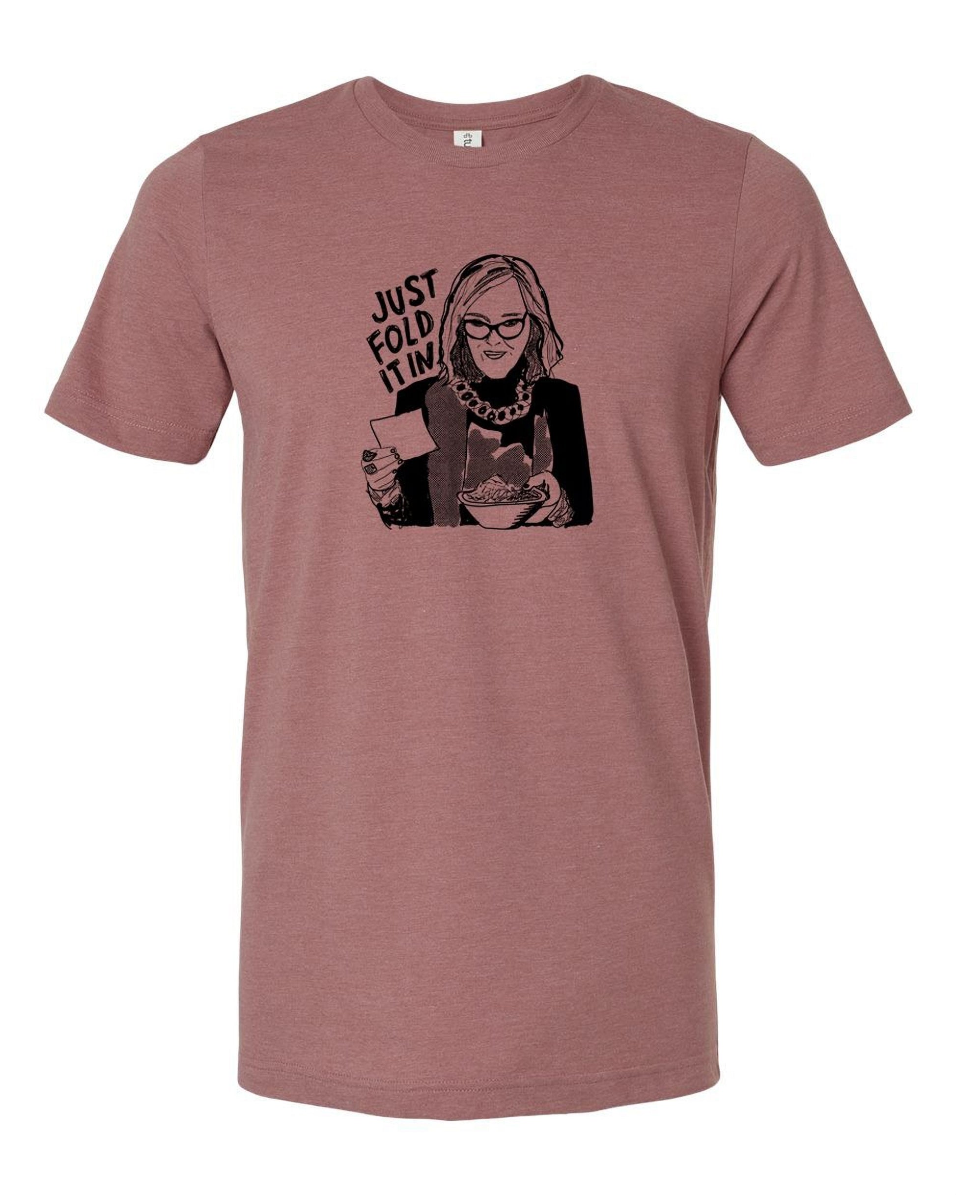 A graphic t-shirt design featuring a woman with glasses and a serious expression, holding a book and a cup of coffee. The text above the image says "JUST FOLD IT".