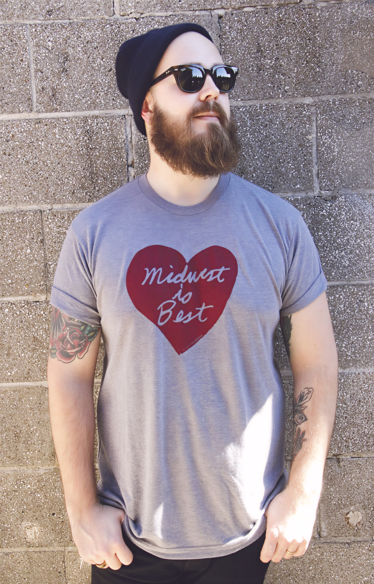 A man with a beard wearing a gray t-shirt with a red heart and the text "Midwest is Best" stands in front of a brick wall.
