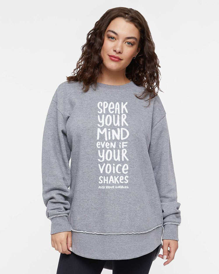 A woman wearing a grey sweatshirt with the text "SPEAK YOUR MIND EVEN IF YOUR VOICE SHAKES" printed on it.