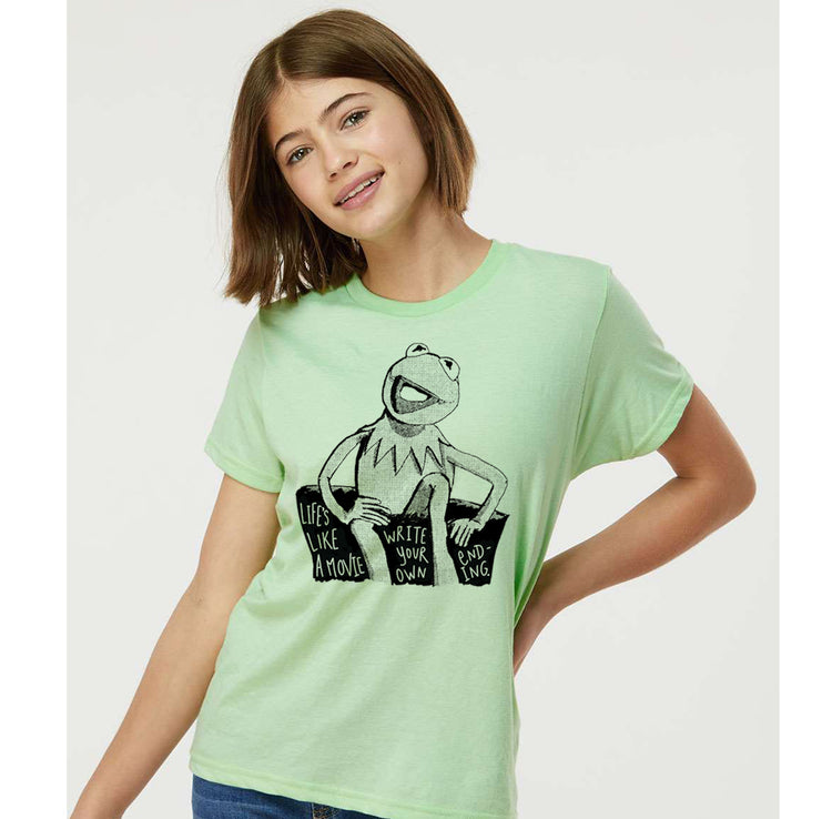A young woman wearing a lime green t-shirt with a graphic of Kermit the Frog and the text "LIVES LIKE A MOVIE" printed on it.
