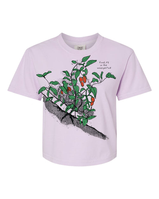 A pink t-shirt with a graphic design depicting a plant with green leaves and red berries.