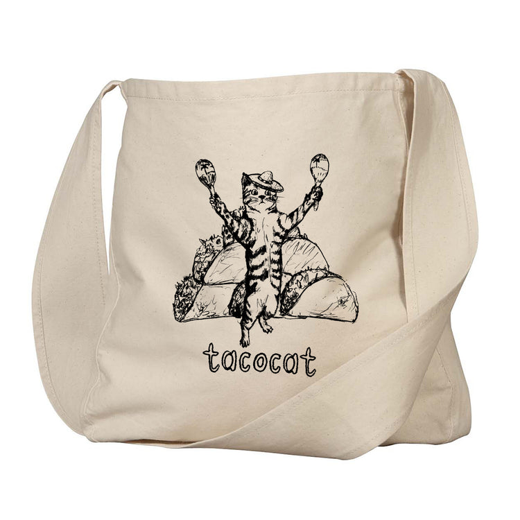 A beige canvas tote bag with a black and white illustration of a cat holding a taco and a burrito, along with the word "tacocat" printed below.