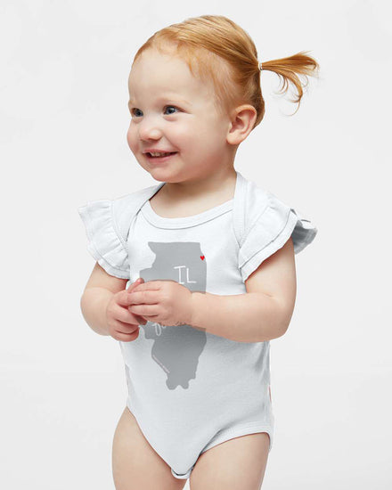 A smiling baby girl wearing a white onesie with a graphic of Illinois on it.
