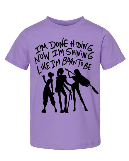 A purple t-shirt with a graphic design featuring silhouettes of three people and text that reads "I'm done hiding now I'm shining like I'm born to be".
